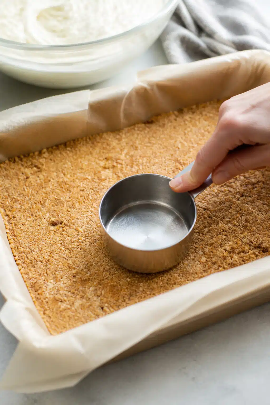 Close-up process shot: the pressed crunchy graham cracker–nut base in a parchment-lined 9x13 pan b