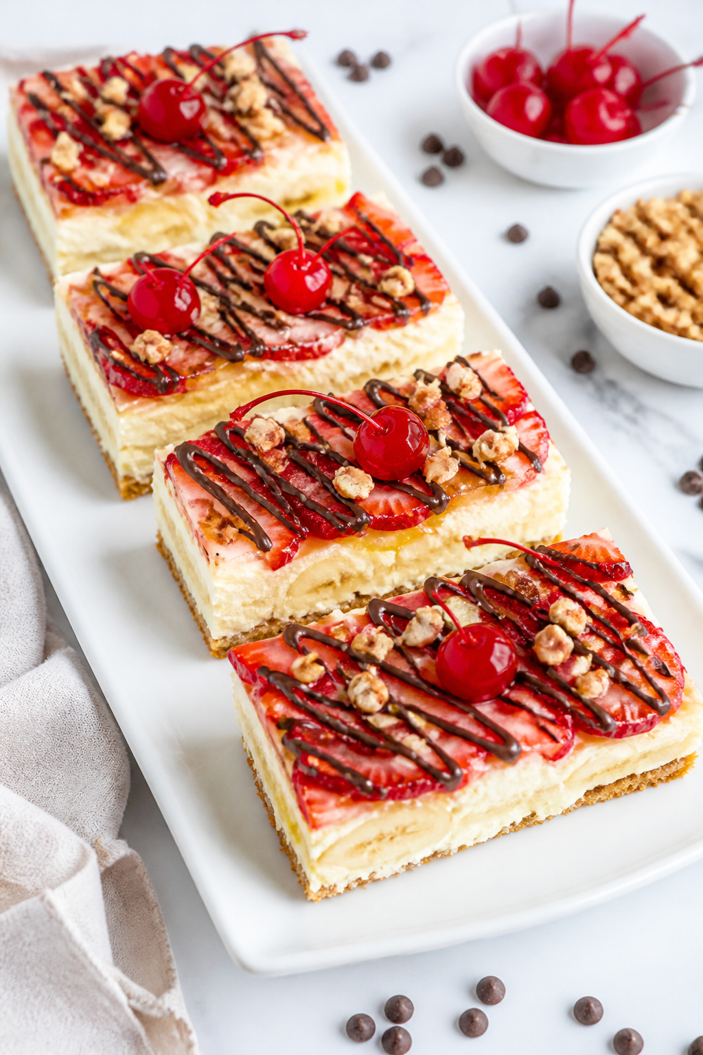 Overhead final presentation: neatly sliced no-bake banana split dessert bars arranged on a white pla