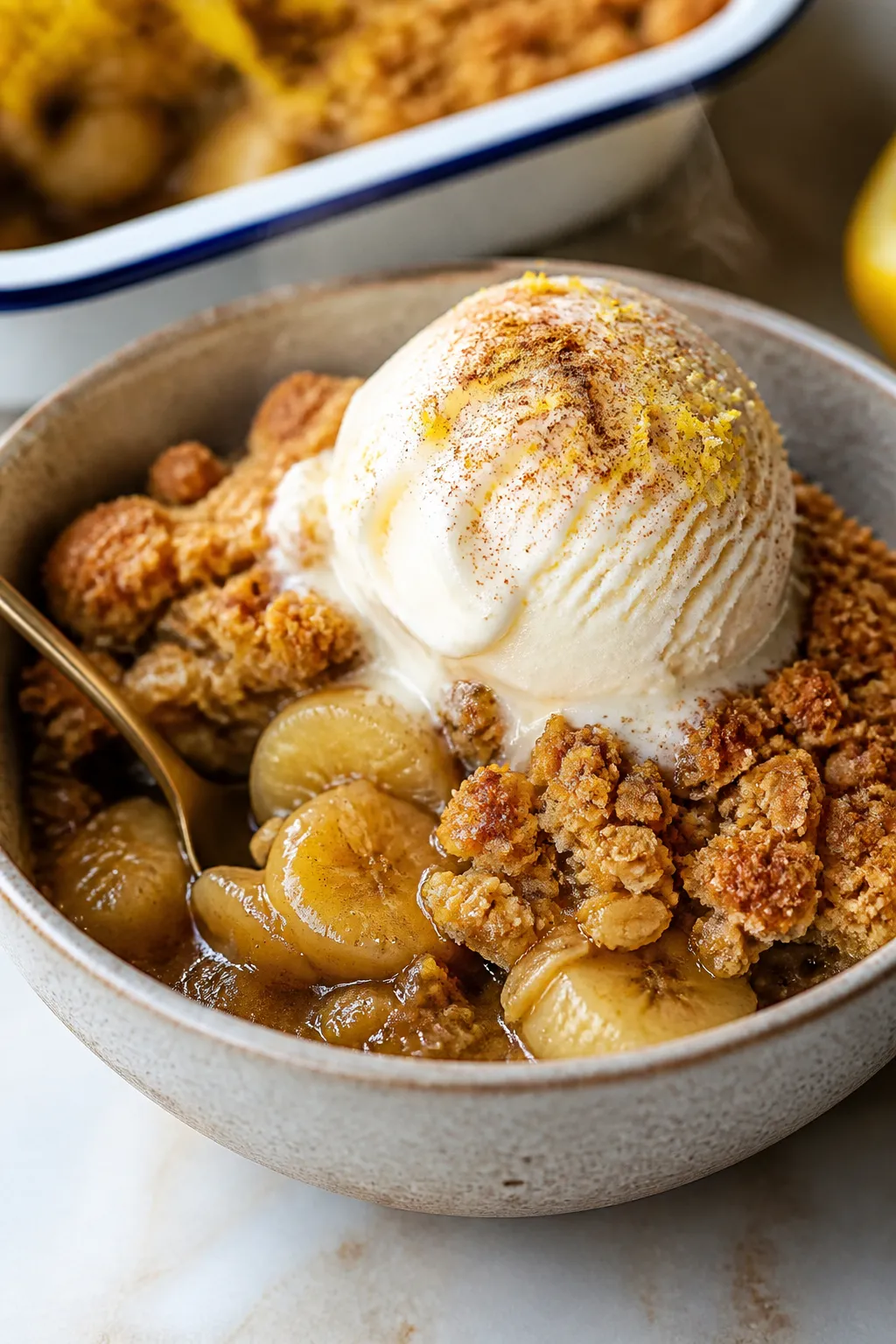 Close-up, of a warm serving of Banana Crumble Bake scooped into a small stoneware bowl, topped with 